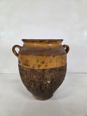 un vase marron muni d'anses, posé sur une surface blanche