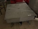 une table en métal au milieu d'une pièce, avec des draps rouges étalés sur le sol