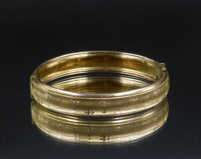 two gold bang bracelets on a black surface with a black background