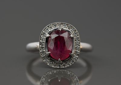 un gros plan d'une bague sertie d'un rubis et de diamants posée sur une surface réfléchissante