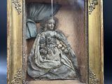 une sculpture antique en bronze représentant une femme tenant un bébé dans ses bras, dans un cadre doré