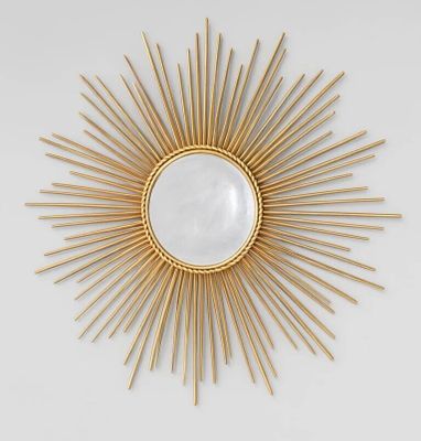 un miroir doré à rayons, accroché au mur à côté d'un mur blanc