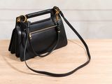 a black leather handbag sitting on top of a wooden table