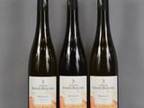 trois bouteilles de vin sont posées sur une table devant un fond gris