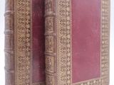 an old book with a red cover sitting on top of a white surface