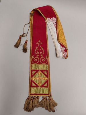 une vieille étole rouge et or ornée de pompons, accrochée au mur