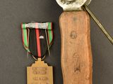 an old wooden knife with a medal on it next to a small metal object