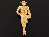 a gold plated pin with a woman in a hat and dress