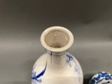 a white vase with a blue and white design next to a blue and white vase with a bird on it