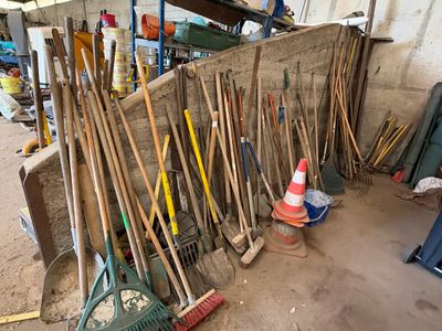 de nombreux balais et râteaux appuyés contre un mur