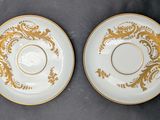 two white and gold plates with gold designs on them on a table