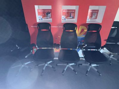 four black office chairs are lined up against a red wall