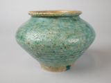 a green vase with a gold lid sitting on a white surface