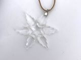 a white snowflake pendant with a brown cord on a white surface