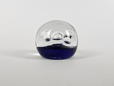 une petite boule de verre avec un socle bleu posée sur une surface blanche