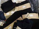 several pairs of black and tan pants with tags on them sitting on a bed