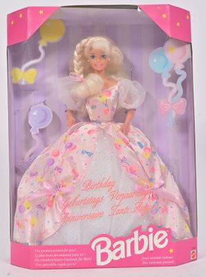 une poupée dans une boîte rose décorée de ballons et de confettis