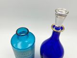two blue glass bottles sitting next to each other on a white surface