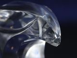 a clear glass sculpture of a bird on a black surface