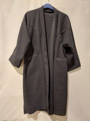 un manteau gris accroché au mur, à côté d'un mur blanc