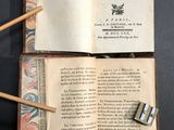 un livre ouvert, d'où sortent des bâtonnets en bois, posé sur une table
