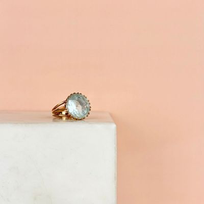 une image représentant une bague en or sertie d'une topaze bleue, posée sur un bloc de marbre