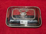 un plat ancien en argent avec un couvercle en verre, posé sur un napperon rouge