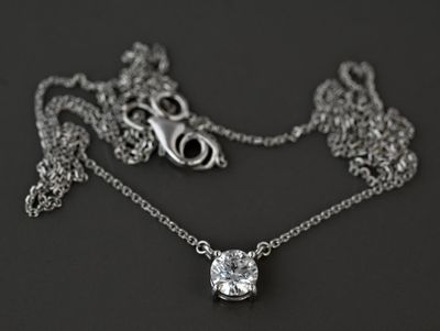 un collier en argent orné d'un diamant, posé sur un fond noir