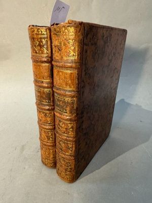 two old books are stacked on top of each other on a white surface