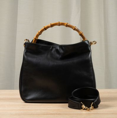 a black leather bag with bamboo handles and a belt on a wooden table