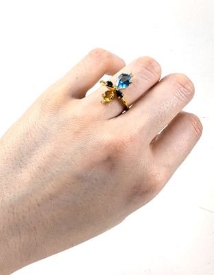 la main d'une femme tenant une bague sertie d'une pierre bleue et jaune