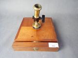 un microscope ancien plaqué laiton, présenté dans un coffret en bois, posé sur une surface grise