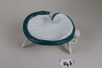 a small white bowl with a green handle on a stand