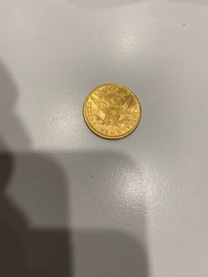 une pièce d'or posée sur une table, à côté de l'ombre d'une personne