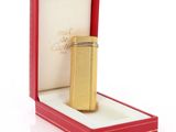 une image représentant un briquet doré dans une boîte rouge posée sur une surface blanche