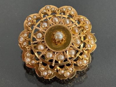 a gold brooch with pearls in it on a black surface