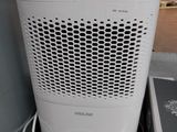 un purificateur d'air blanc posé par terre à côté d'une pile de cartons