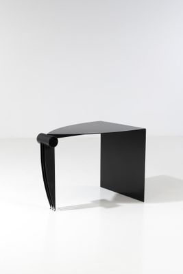 une table noire au plateau incurvé, posée sur un socle blanc