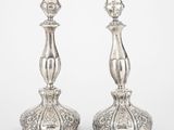 une paire de bougeoirs en argent posés sur un socle, sur fond blanc
