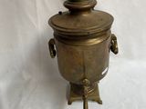 théière ancienne en laiton avec couvercle, posée sur un socle, sur fond blanc