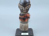 statue représentant la tête d'un homme, posée sur un socle en bois, avec un foulard rouge autour du cou