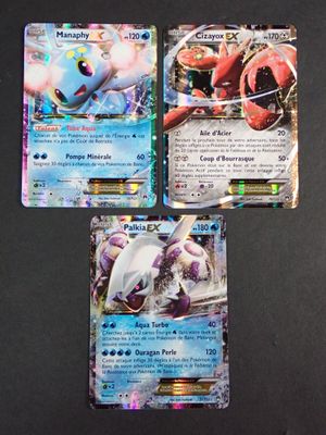 Trois cartes Pokémon sont posées sur une table avec un fond noir.