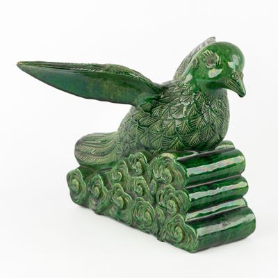 une statue d'oiseau vert posée au sommet d'une pile de livres