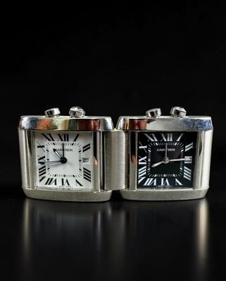 two silver square watches sitting side by side on a black surface