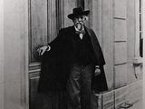 black and white photograph of a man in a top hat and coat leaning against a door