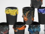 six black cups with different colored designs on them on a white surface