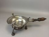 une assiette ancienne en argent avec un manche en bois, posée sur une surface blanche