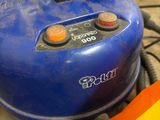 a blue air compressor sitting on the floor next to a yellow bag