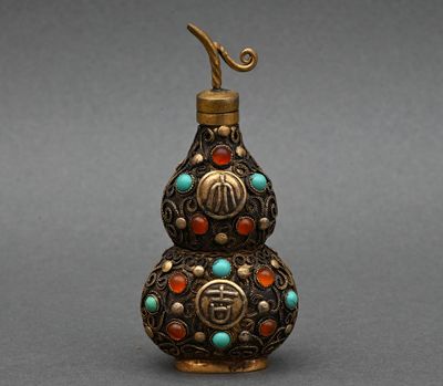 une vieille bouteille en laiton ornée de perles turquoise, rouges et vertes