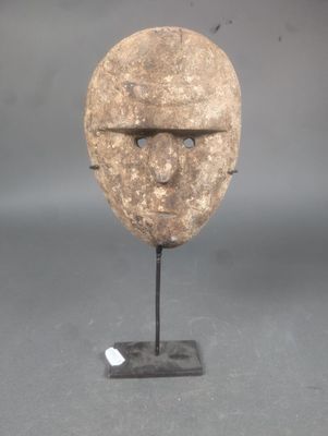 une image représentant un masque en pierre posé sur un socle, sur une surface grise